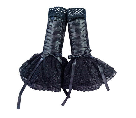 ein Paar Damen Armstulpen mit Röckchen und Zier Schnürung in Kuro Lolita schwarz mit breiter Satinband Korsett-Bondage-Schnürung. Hübsche Abschluss Spitze am Oberarm und am Rock mit Zierspitze veredelt. Die Stulpen stehen hier an der Wand. Die Bänder sind zu einer Schlaufe gebunden.