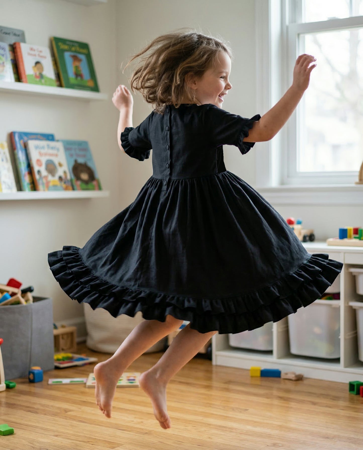 Kind trägt schwarzes Akari Kleid von Mouska Alfar aus hochwertiger Baumwolle und hüpft dabei so dass der ausladende Rock weit schwingt. Kleid auch gut zum Tanzen geeignet. Flamenco, Salsa, klassik und Kindertanz.