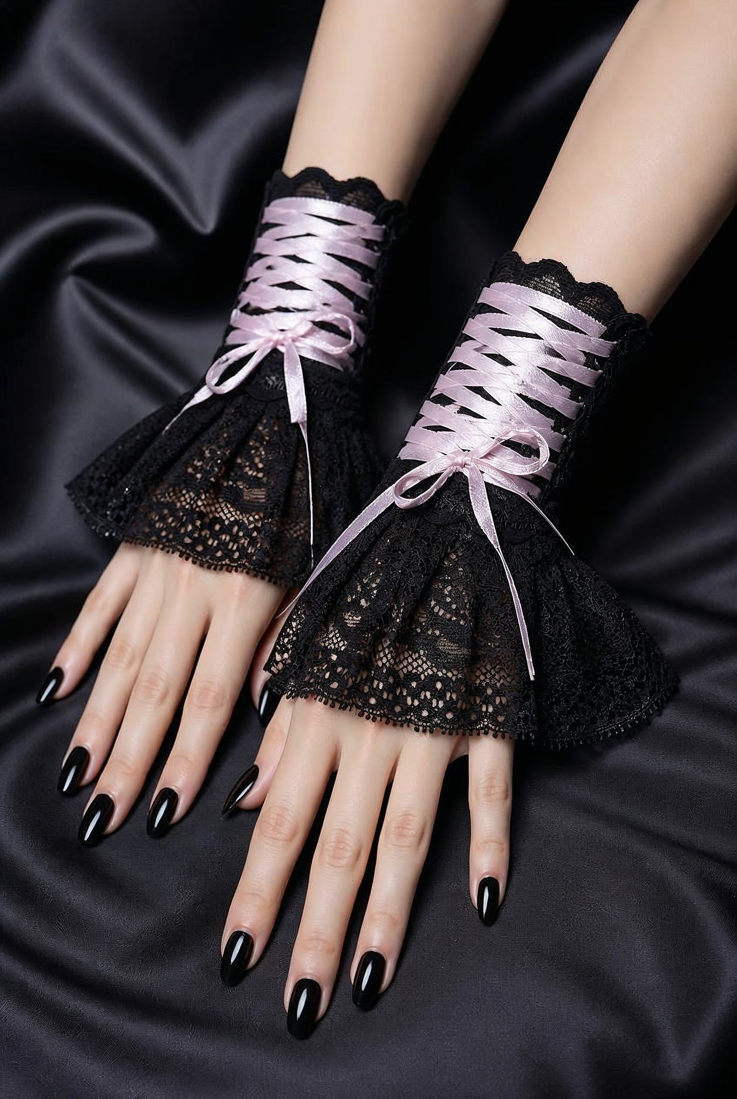 ein Paar Gothic Armstulpen von Mouska Alfar Hamburg, im Darkmode Aesthetic Punk Style auf schwarzen Stoffen an Damen händen fotografiert, die nebeneinander liegen. Finger mit schwarzem Nagellack, die Schnürung auf den Manschetten ist geschnürt und mit Schleife verschlossen.