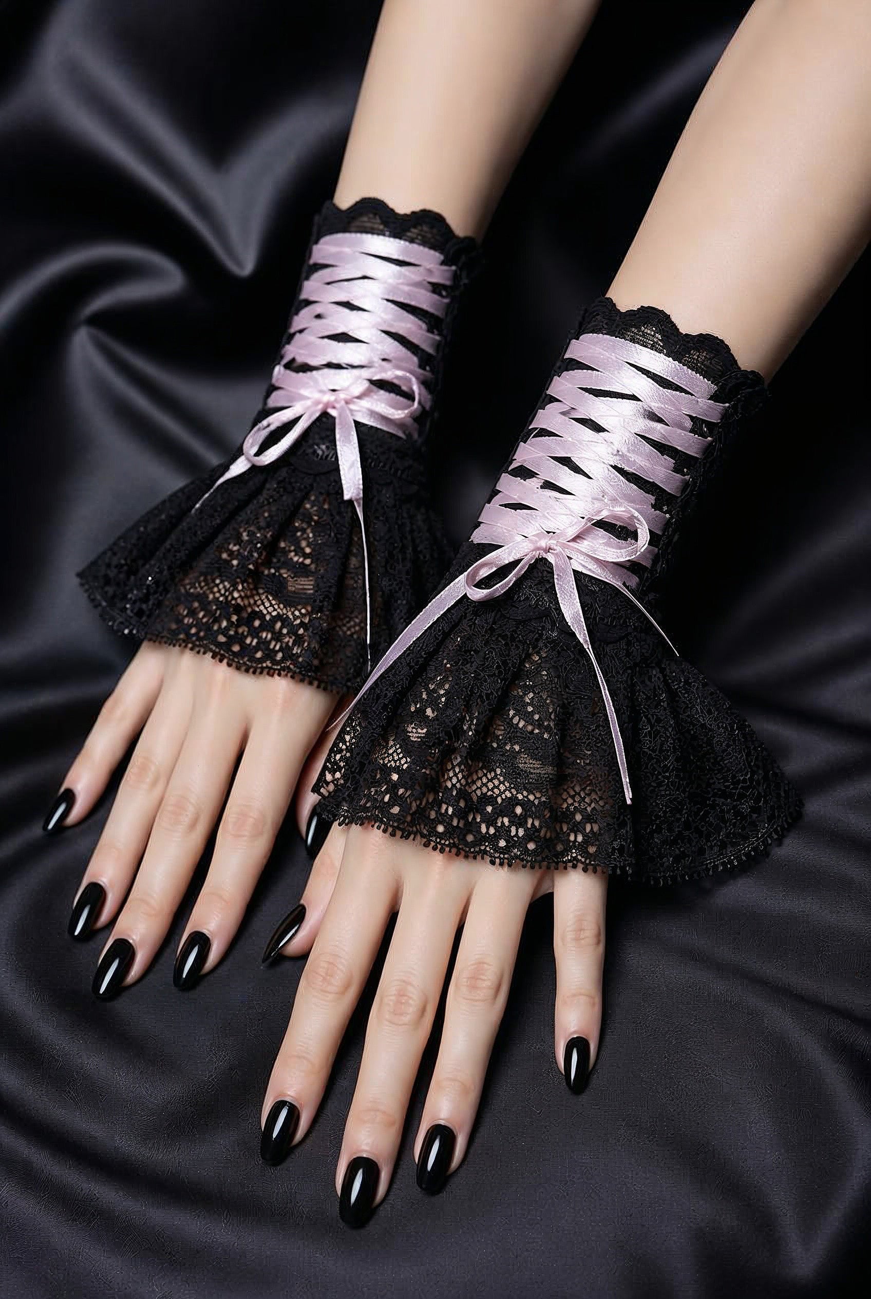 ein Paar Gothic Armstulpen von Mouska Alfar Hamburg, im Darkmode Aesthetic Punk Style auf schwarzen Stoffen an Damen händen fotografiert, die nebeneinander liegen. Finger mit schwarzem Nagellack, die Schnürung auf den Manschetten ist geschnürt und mit Schleife verschlossen.