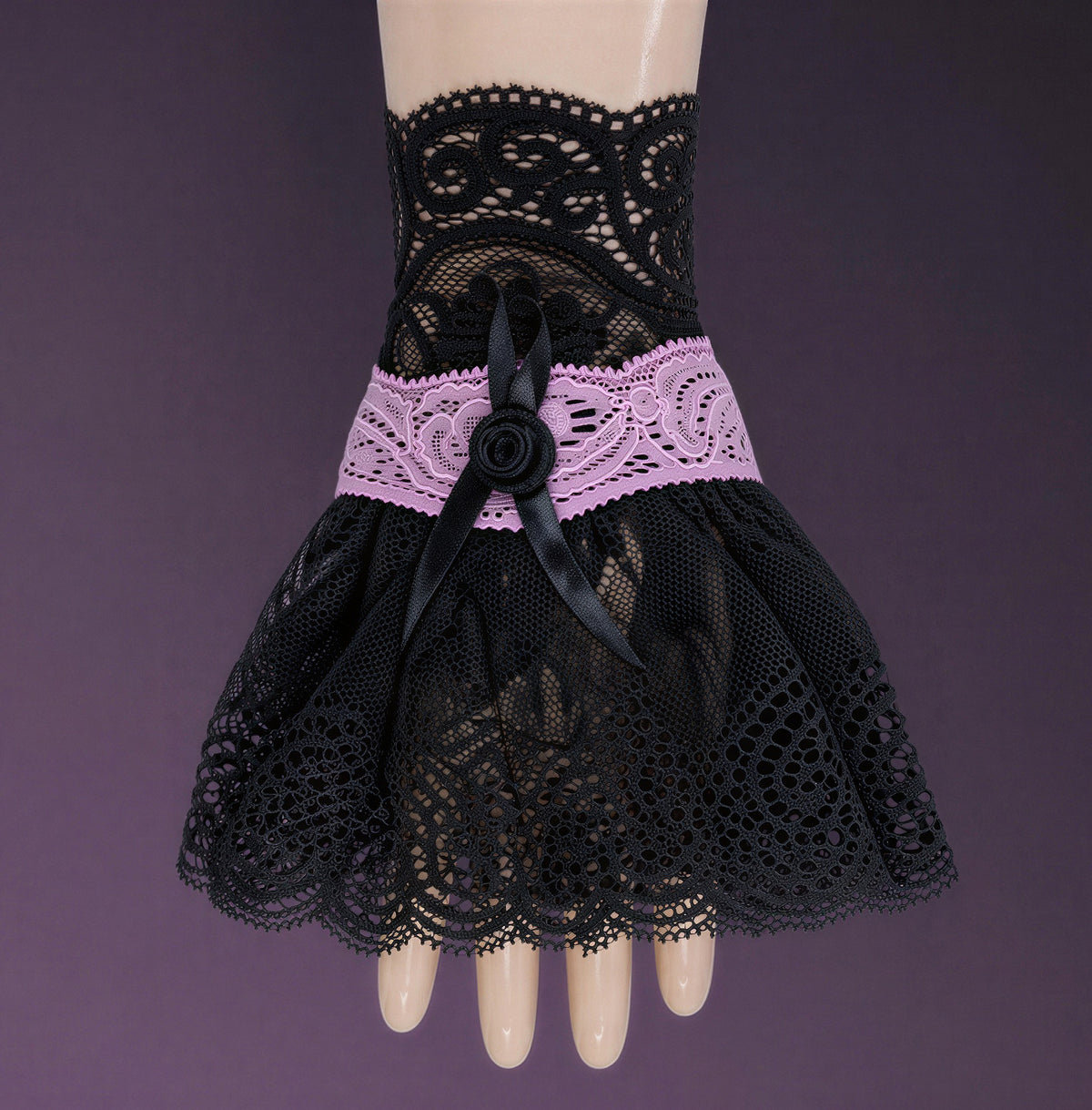 eine einzelne edle gothic Manschette / Armstulpe in schwarz rosa an einer Puppen Modell Hand im Stehen fotografiert. Sie füllt das ganze Bild aus. Hintergrund rosa schwarz.