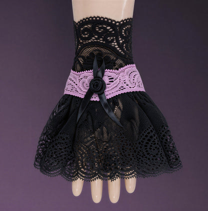eine einzelne edle gothic Manschette / Armstulpe in schwarz rosa an einer Puppen Modell Hand im Stehen fotografiert. Sie füllt das ganze Bild aus. Hintergrund rosa schwarz.