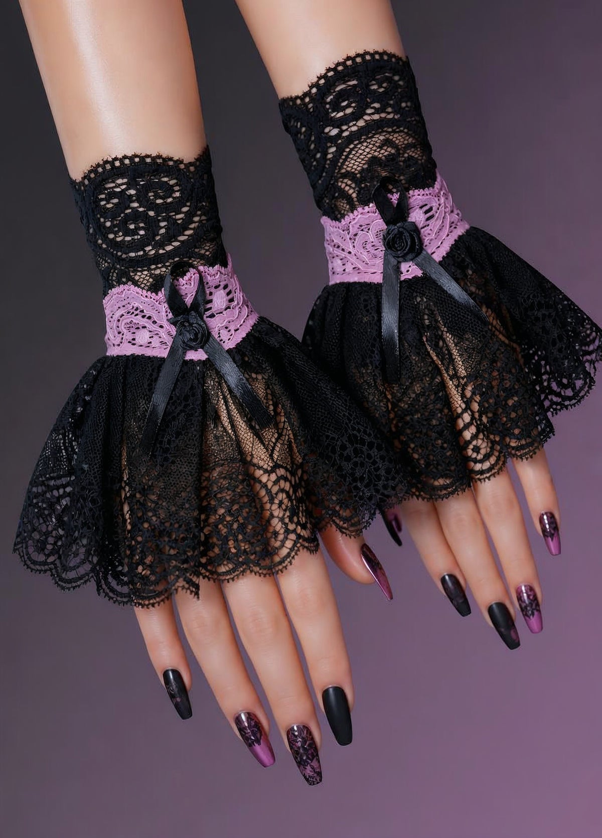 Manschetten/Armstulpen gothic lolita in schwarz rosa mit schwingendem Röckchen aus elastischen und unelastischen Nobel Spitzen, hervorragende Qualität aus deutscher Produktion. Fotografiert an Damen Händen mit kunstvoll gestalteten Fingernägeln. Ambiente schwarz lila