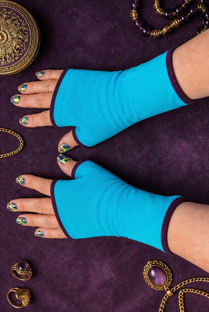 ein Paar Damen unisex Handschuhe aus Baumwolle Jersey mit Paspel, gefüttert. Oberstoff türkis, Futter aubergine, dunkel violett. An Damenhänden fotografiert die seitlich im Bild liegen und das ganze Foto ausfüllen, mit schönen bunt lackierten Fingernägeln. Hintergrund Purple Lila Vintage Ambiente