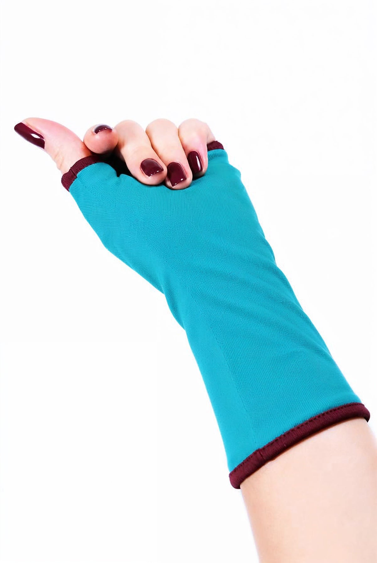 Einzel Basic Handschuh ohne Finger, fotografiert an einer Damenhand, die auf dem Tisch liegt. Bunt lackierte Fingernägel, sehr stylisch und exklusiv. Hintergrund Studio weiss. Aus Baumwolle Jersey mit Paspel, gefüttert. Oberstoff türkis, Futter bordeaux wein rot.