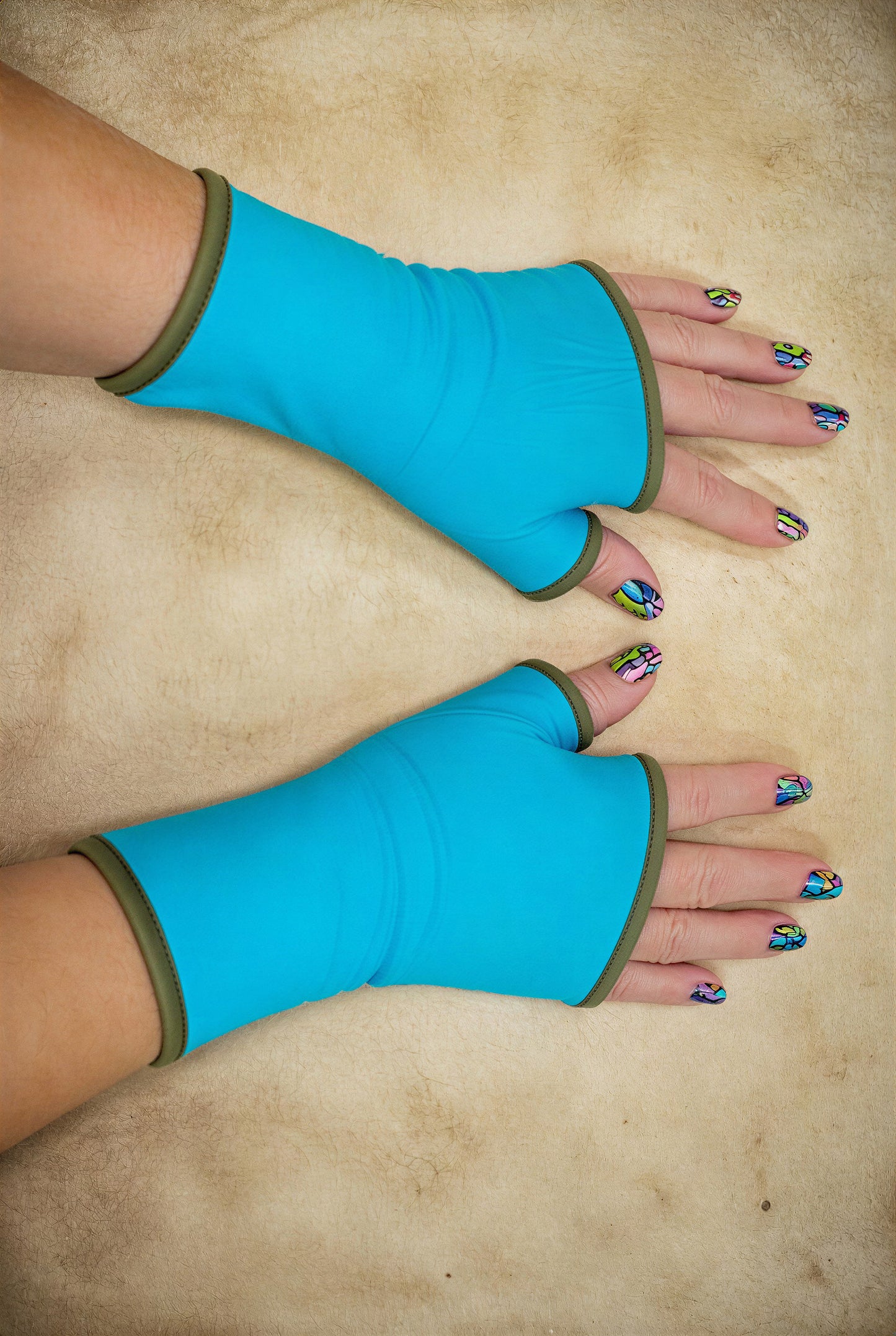 ein Paar Damen unisex Handschuhe aus Baumwolle Jersey mit Paspel, gefüttert. Oberstoff türkis, Futter khaki oliv gruen. An Damenhänden fotografiert die seitlich im Bild liegen und das ganze Foto ausfüllen, mit schönen bunt lackierten Fingernägeln.