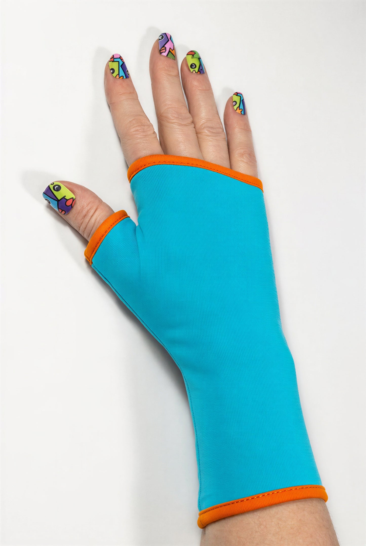 Einzel Basic Handschuh ohne Finger, fotografiert an einer Damenhand, die auf dem Tisch liegt. Bunt lackierte Fingernägel, sehr stylisch und exklusiv. Aus Baumwolle Jersey mit Paspel, gefüttert. Oberstoff türkis, Futter orange.