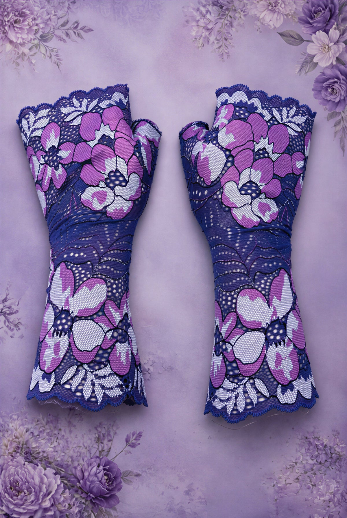 ein Paar Damen Spitze Handschuhe fingerlos mit großen Blumen in violett magenta liegen in flatlay mitten im Bild auf Vintage Ambiente Lila Flieder Hintergrund.
Handarbeit von Mouska Alfar