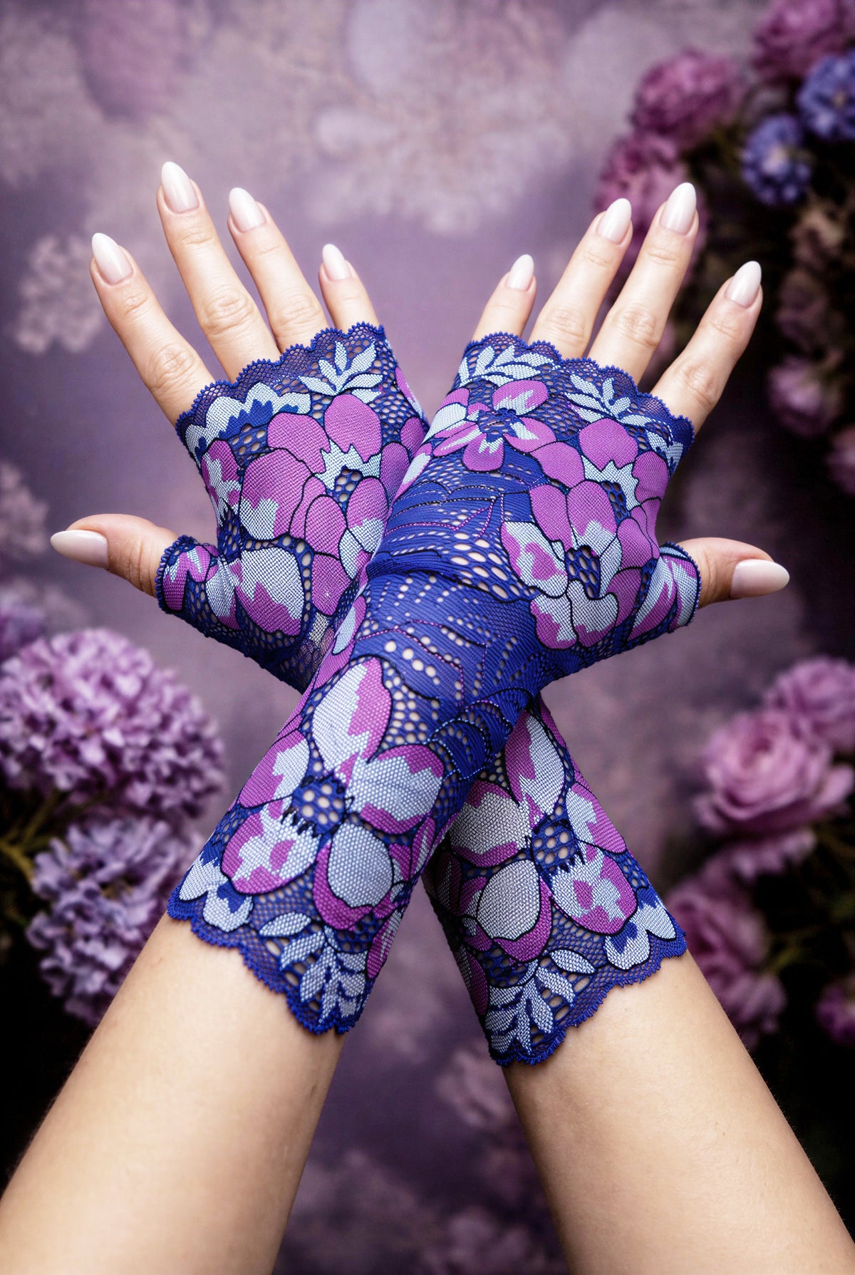 ein Paar lange Boho Hippie Handschuhe in lila blau Tönen übereinander gekreuzt mittig auf dem Foto, lackierte Fingernägel. Die Handschuhe kommen schön zur Geltung. Sie sind vom Grundtenor dunkelblau-violett mit riesigen verstreuten Blumen. Aus Wäschespitze gearbeitet, satte Farben, wunderhübsch.