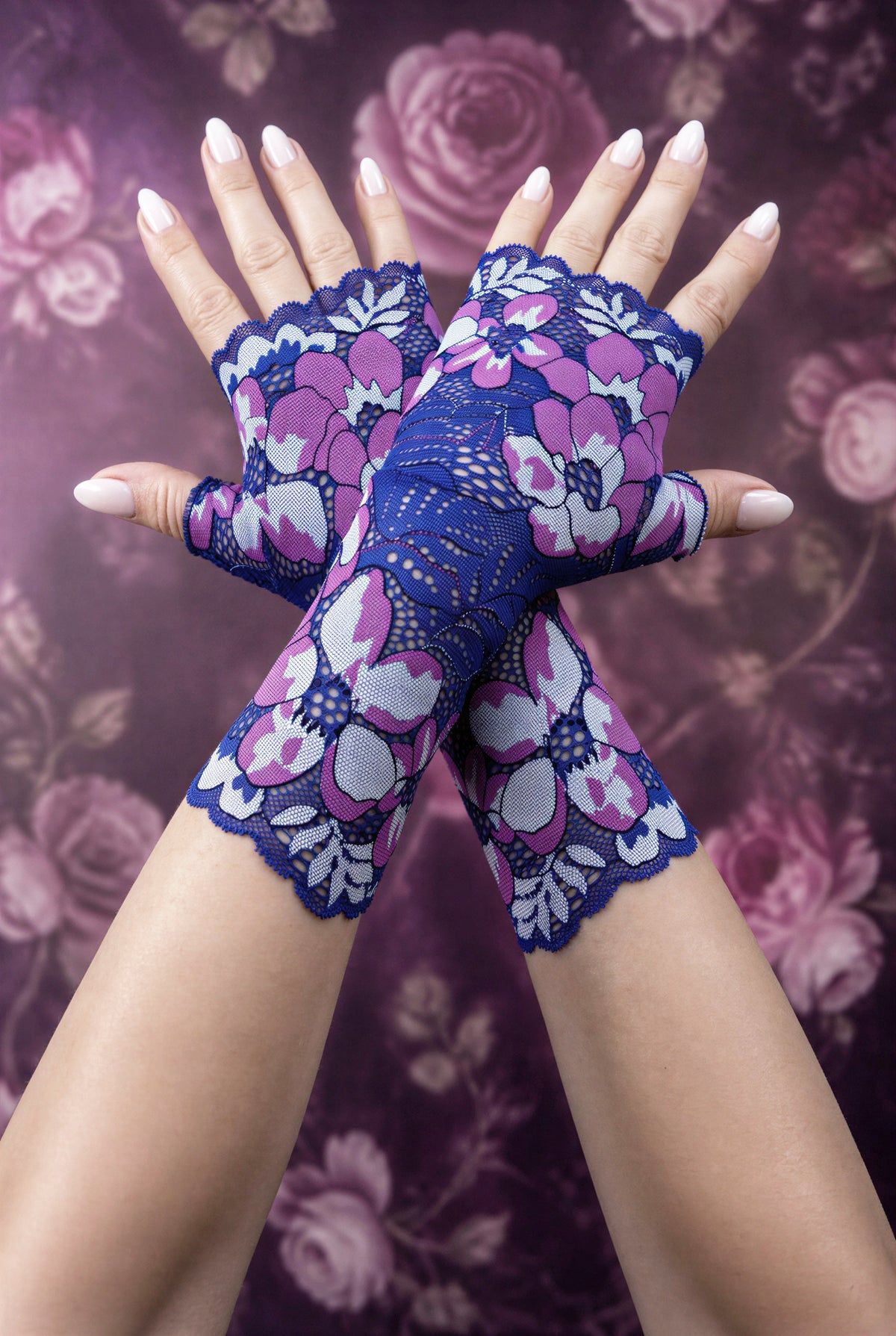 ein Paar lange Boho Hippie Handschuhe in lila blau Tönen übereinander gekreuzt mittig auf dem Foto, lackierte Fingernägel. Die Handschuhe kommen schön zur Geltung. Sie sind vom Grundtenor dunkelblau-violett mit riesigen verstreuten Blumen. Aus Wäschespitze gearbeitet, satte Farben, wunderhübsch.