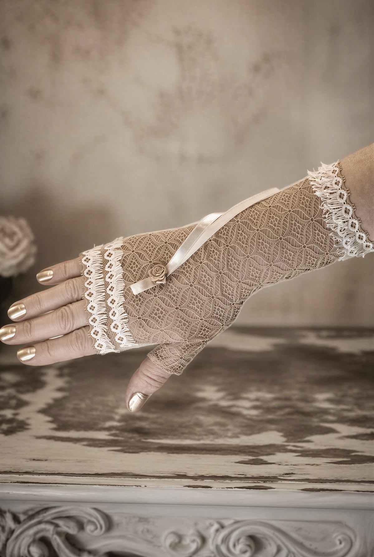 Damen Hippie Handschuh fingerlos, lang mit Boho Fransen Borte, Schleife+Rose Verzierung im Chabby Landhaus in beige weiss. Eine Damenhand trägt den Handschuh. Im Hintergrund Vintage Ambiente