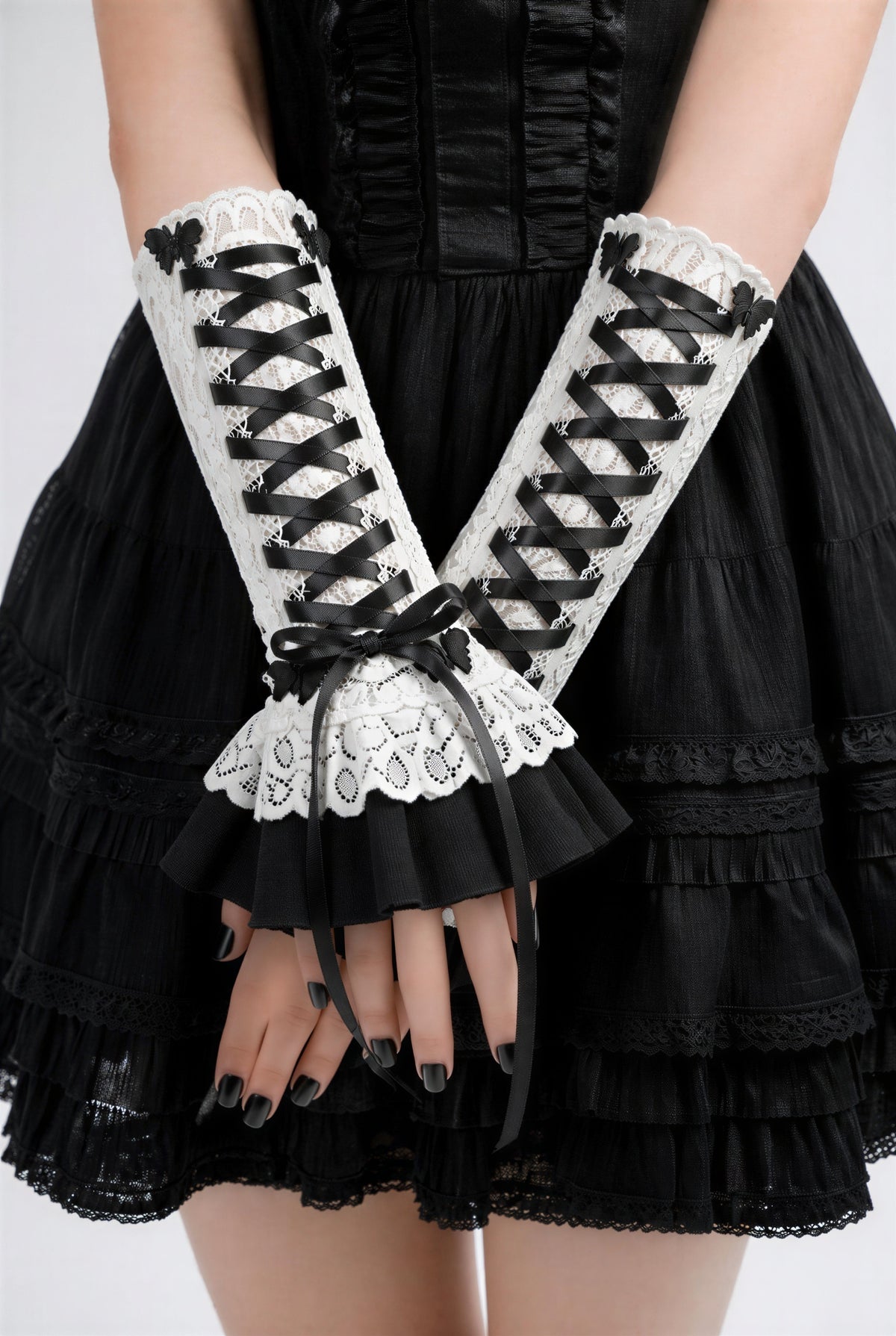 Harajuku Dark Sweet Kawaii Stulpen mit Zierschnürung an einer Dame präsentiert. Sie steht im Bild und schlägt ihre Arme übereinander, die Fingernägel schwarz lackiert. Die Hand,-Armschmuck-Stulpen reichen ihr bis fast an den Ellbogen. Sie sind an sich etwas kürzer, 24 cm lang.