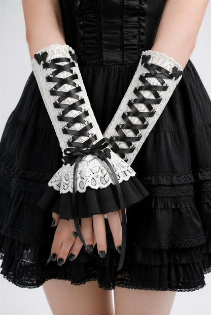 Harajuku Dark Sweet Kawaii Stulpen mit Zierschnürung an einer Dame präsentiert. Sie steht im Bild und schlägt ihre Arme übereinander, die Fingernägel schwarz lackiert. Die Hand,-Armschmuck-Stulpen reichen ihr bis fast an den Ellbogen. Sie sind an sich etwas kürzer, 24 cm lang.
