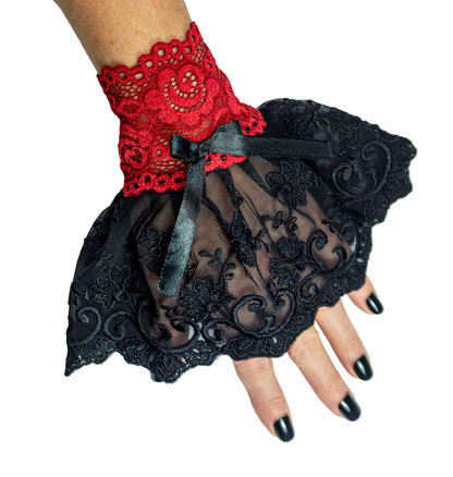 rote Manschetten aus elastischer weicher Textronic Spitze + schwarze Satin Schleife verziert, mit Röckchen aus bestickter, edler Netz-Spitze in schwarz, dicke Qualität höchster Ansprüche - slow fashion hergestellt in Deutschland. Verschiedene Größen von XS bis XL für kleine bis große Hände, die Länge bleibt dabei statisch. Abgebildet ein einzelner Pulswärmer, Manschette, Stulpe an einer Frauen Hand.