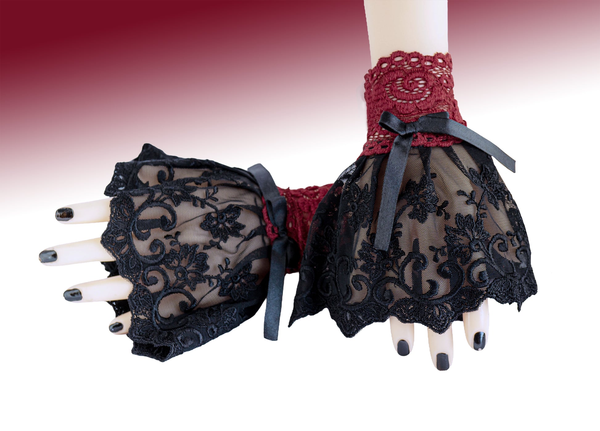 Manschetten aus Spitze in schwarz rot, fotografiert an einem Paar Damen Hände, die übereinander liegen. Schwarz lackierte Fingernägel. Kleine Armstulpen mit Schleife aus Satin verziert, Handgefertigt in Deutschland. Sehr hohe Qualität. Gesamte Produktionskette vor Ort in Deutschland.
