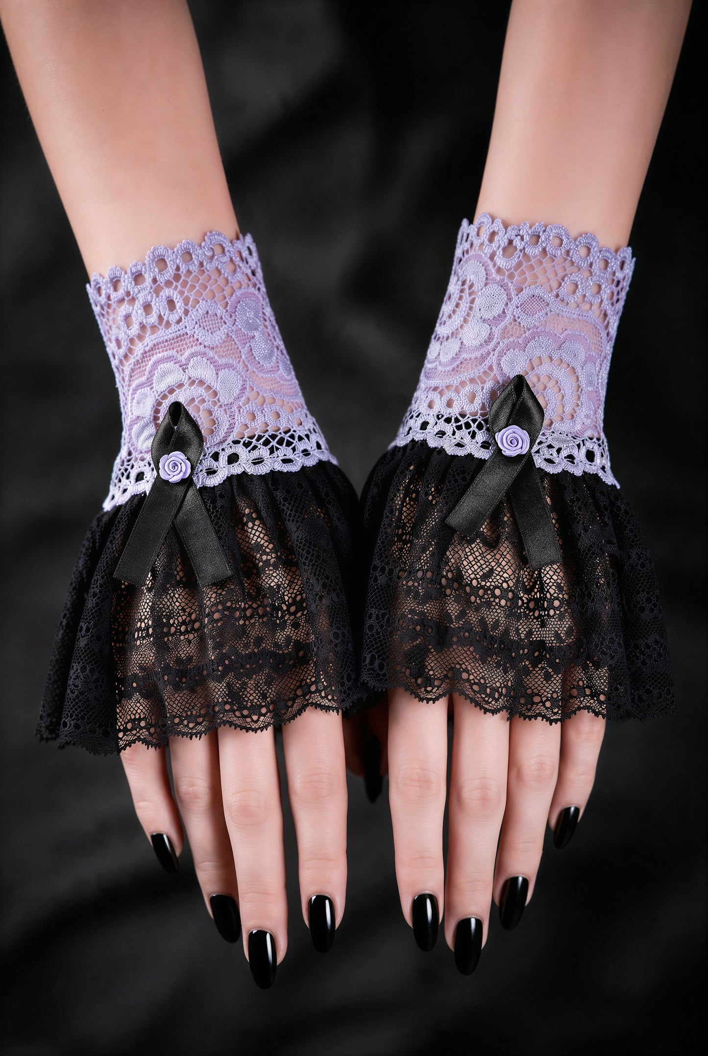 Sweet Lolita Gothic Manschetten aus Spitze in flieder schwarz, fotografiert an einem Paar Damen Hände, die auf schwarzen Stoff nebeneinander liegen. Schwarz lackierte Fingernägel. Kleine Armstulpen mit Satin Rose verziert, Handgefertigt in Deutschland.