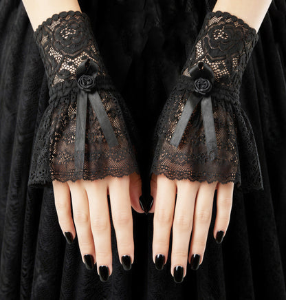 ein paar gothic Manschetten an Damen Händen präsentiert, schwarz lackierte Fingernägel. Hintergrund gothic ambiente. Stulpen in schwarz mit Röckchen leicht schwingend und Manschetten Spitze mit Rosenmuster und Satinband mit Rose verziert.