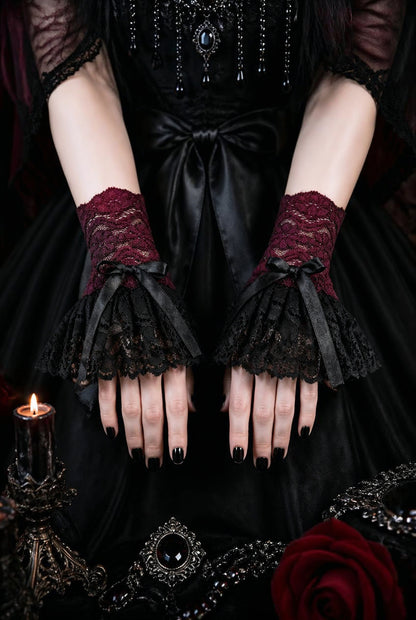 ein paar gothic Manschetten an Damen Händen präsentiert, Hintergrund gothic vampir ambiente. Stulpen in schwarz bordeaux-rot mit ausladendem schwingenden Röckchen und manschetten teil mit satin schleife verziert.