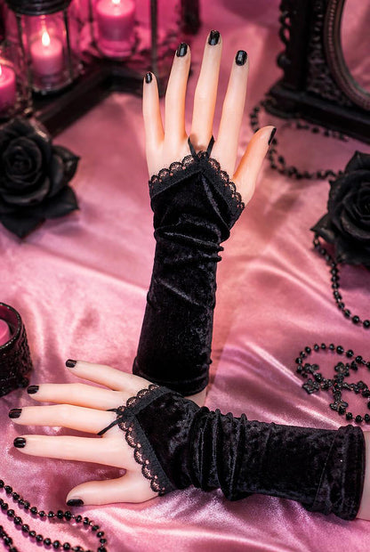 ein weiteres Paar schwarze Wichtel-Stulpen. An Puppenhänden fotografiert. Eine Stulpe stehend, eine liegend, Nägel schwarz lackiert. Hintergrund gothic ambiente in rot schwarz