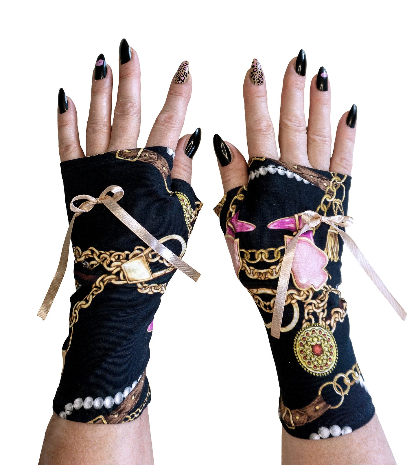 ein paar Handschuhe ohne Finger, fotografiert an Damen Händen mit langen lackierten Fingernägeln. Die schmückenden Pulswärmer sind aus Baumwolle Jersey mit Digitaldruck Accessoires, Schmuck wie Halsketten, Ohrringe und Broschen in gold rosa beige Tönen auf schwarzem Grund.