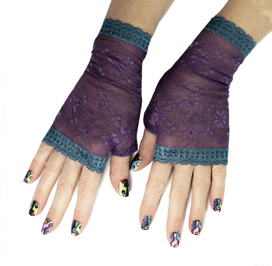 ein Paar Damen Handschuhe in violetter Spitze aus deutscher Produktion mit türkis farbiger Bogenkante, fotografiert an weiblichen Händen mit buntem Nagellack mosaik Muster. 
Die Handstulpen haben keine Finger, einen halben Daumen. Handarbeit aus dem Hause Mouska Alfar. 