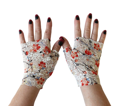 ein paar Handschuhe ohne Finger an Damenhänden fotografiert, man sieht die ganzen Hände frontal, lackierte Fingernägel. Sie sind aus Spitze gefertigt im japan Stil mit Kirschblüten, Sakura auf weißem Grund. Eine rechte und eine linke Hand.