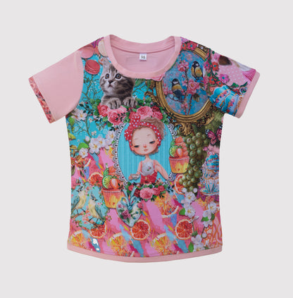 Flatlay Fotografie von rosa kurzärmeliges T-Shirt mit buntem Grafikdruck. Das Design zeigt eine Puppe, ein Hündchen, Cupcakes, Blumen und Vögel. Das Shirt hat einen runden Ausschnitt und ein Größenetikett.In Kindergrößen ab 98 erhältlich.