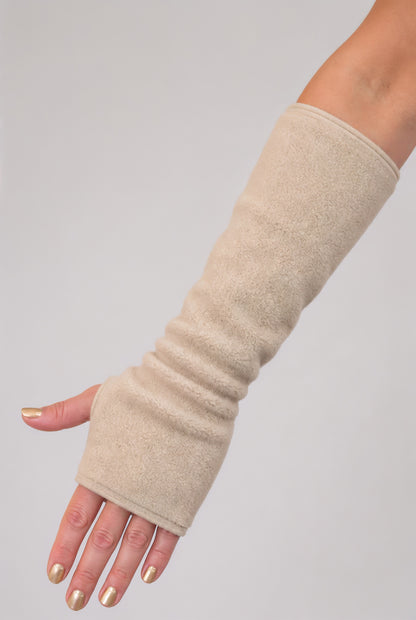 eine Fleece Armstulpe dargestellt an einem Frauenarm. Die Stulpen reichen bis an die Fingerknöchel über die Hand, ohne Finger, fingerlos, aber mit Daumenloch zum rein schlüpfen und bis über den Unterarm hinauf fast bis zur Elle. Material ist flauschig, fluffig und wärmend. Farbe beige.