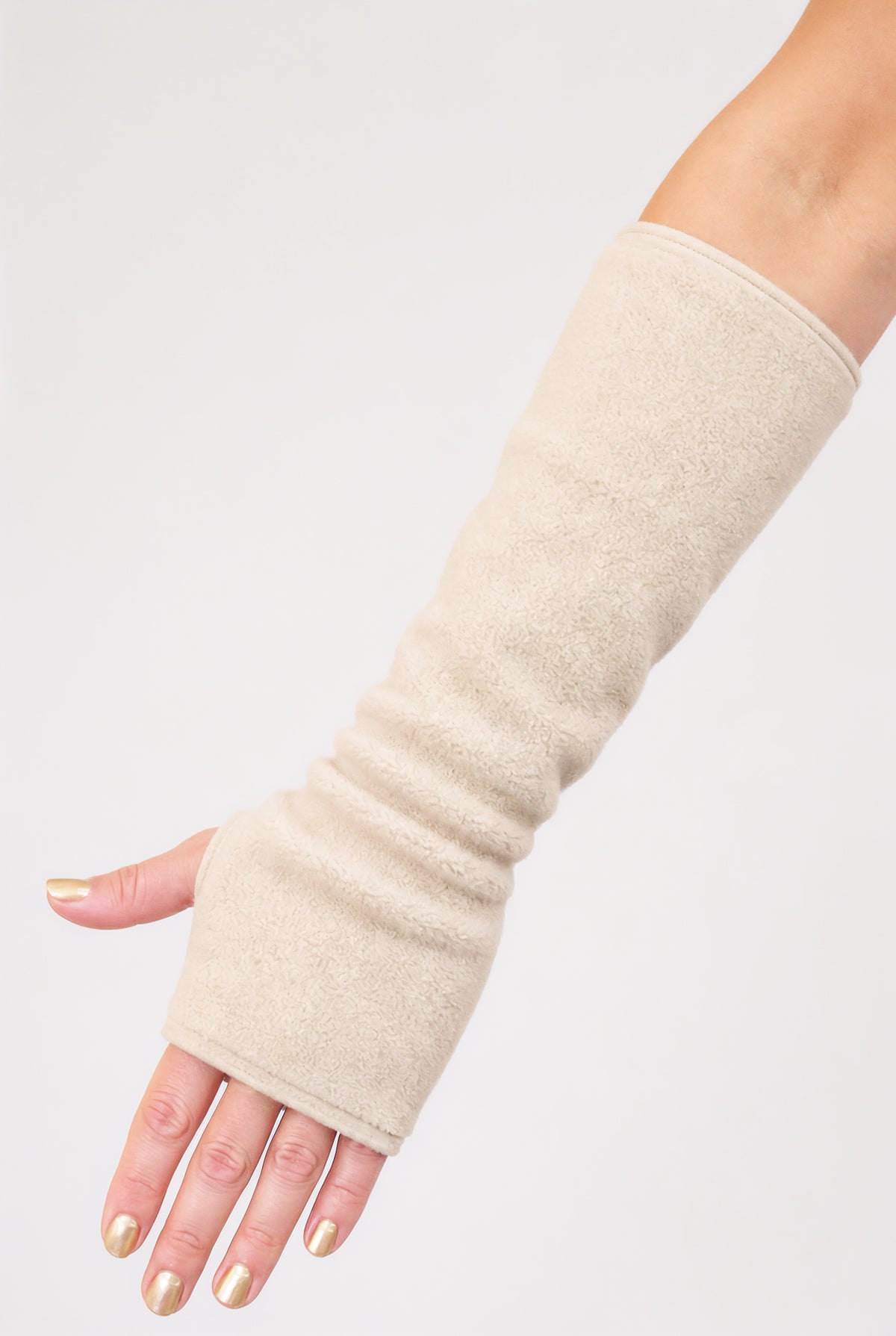eine Fleece Armstulpe dargestellt an einem Frauenarm. Die Stulpen reichen bis an die Fingerknöchel über die Hand, ohne Finger, fingerlos, aber mit Daumenloch zum rein schlüpfen und bis über den Unterarm hinauf fast bis zur Elle. Material ist flauschig, fluffig und wärmend. Farbe beige.