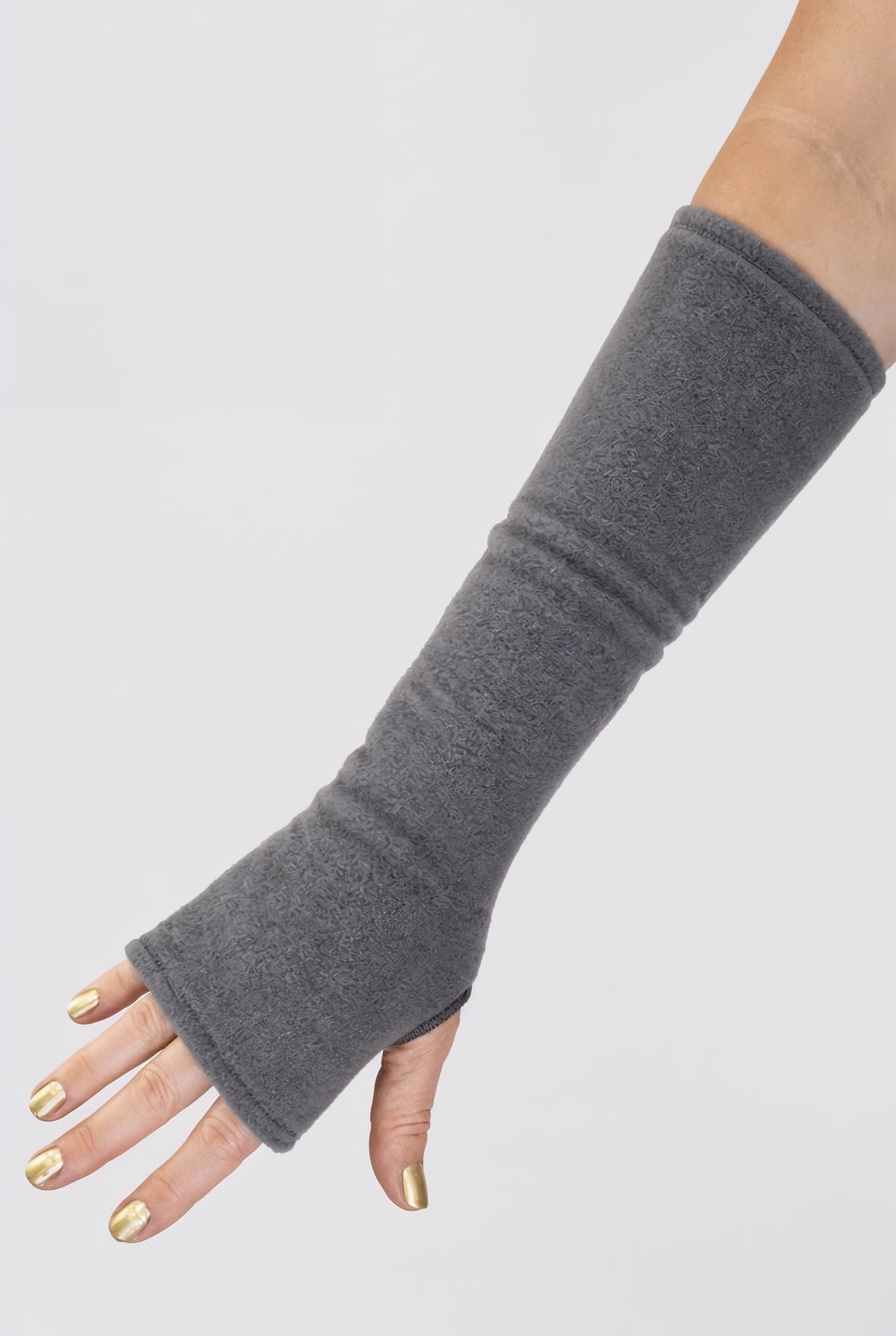 eine Fleece Armstulpe dargestellt an einem Frauenarm. Die Stulpen reichen bis an die Fingerknöchel über die Hand, ohne Finger, fingerlos, aber mit Daumenloch zum rein schlüpfen und bis über den Unterarm hinauf fast bis zur Elle. Material ist flauschig, fluffig und wärmend. Farbe grau.
