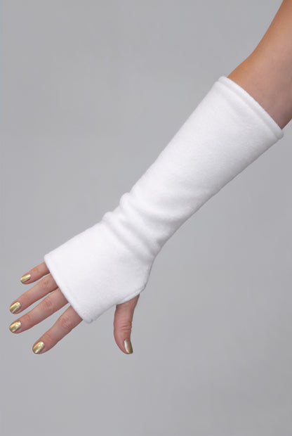 eine Fleece Armstulpe dargestellt an einem Frauenarm. Die Stulpen reichen bis an die Fingerknöchel über die Hand, ohne Finger, fingerlos, aber mit Daumenloch zum rein schlüpfen und bis über den Unterarm hinauf fast bis zur Elle. Material ist flauschig, fluffig und wärmend. Farbe weiß.